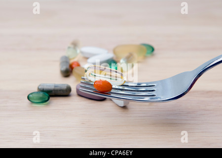 Selection of vitamins (omega 3, Co-enzyme Q10, peppermint, chondroitin, ginkgo and ginseng) on fork and wooden chopping board Stock Photo