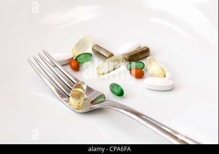 Selection of vitamins (omega 3, Co-enzyme Q10, peppermint, chondroitin, ginkgo and ginseng) with fork on white background. Stock Photo
