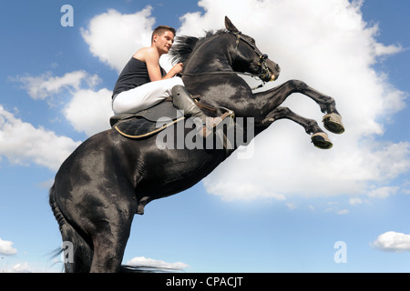 young man and her beautiful black stallion rearing up Stock Photo
