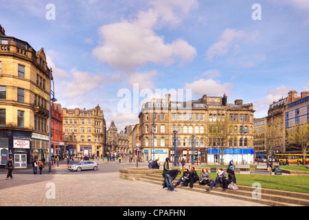 A group of young people sitting on the steps in front of Bradford Town Hall, surrounded by the city's sandstone architecture. Stock Photo