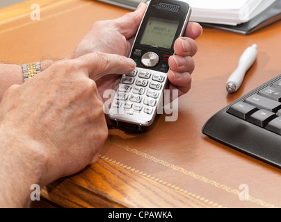Caucasian man pressing buttons on wireless phone on leather desk Stock Photo