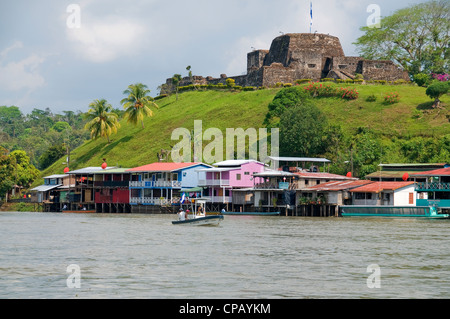 A Nicaraguan tarpon fishing boat trolls the Rio San Juan near the quaint El Castillo fort that overlooks the action from above. Stock Photo