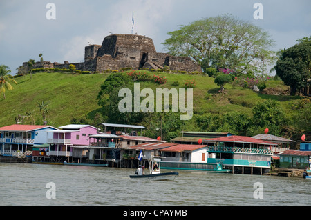 A Nicaraguan tarpon fishing boat trolls the Rio San Juan near the quaint El Castillo fort that overlooks the action from above. Stock Photo