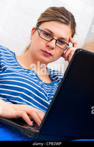 Young pensive woman using laptop and relaxing on sofa. Stock Photo