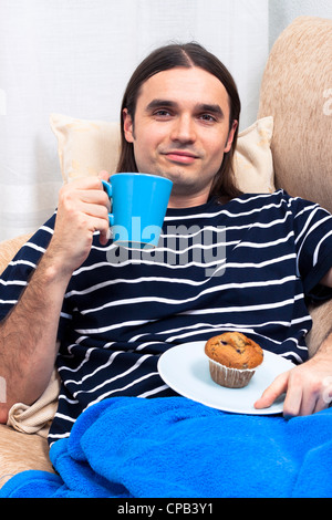 Young man having breakfast and relaxing on sofa. Stock Photo