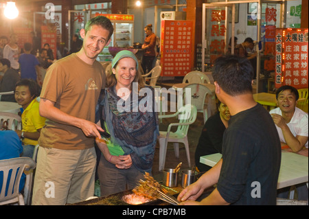 2 European tourists buy food from an outdoor street market vendor in Pingliang. Stock Photo