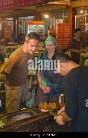 2 European tourists buy food from an outdoor street market vendor in Pingliang. Stock Photo