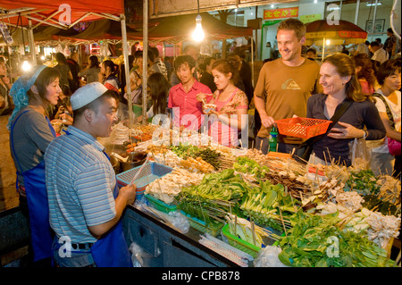2 european tourists buying snack food at the well known Zhengning Road night food street market in Lanzhou. Stock Photo