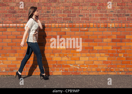 Young woman walk beside the red brick wall while talking on the phone Stock Photo