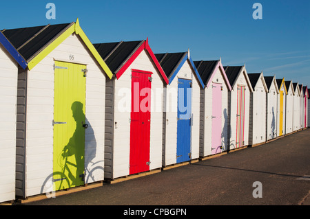 Cyclist shadows on a row of colourful beach huts against blue sky. Goodrington, Paignton, Devon, England Stock Photo