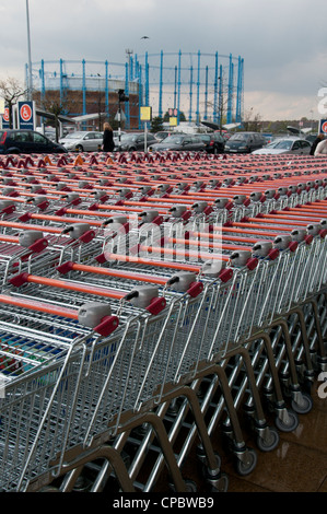 Empty trolleys lined up outside supermarket with gasometer in background Stock Photo