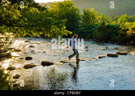 Walker crossing stepping stones on the River Esk near Boot in the English Lake District Stock Photo