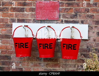 Three bright red fire buckets hanging on a brick wall Stock Photo