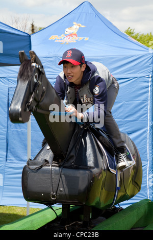 Young Chinese man riding a training horse model, Newmarket festival of Sports, Suffolk East Anglia UK Stock Photo