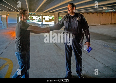 a Hispanic Santa Ana, CA, police officer shakes hands with the appreciative owner of a car that was broken into and robbed. Stock Photo