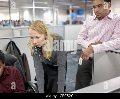 Two workers looking over the shoulder of their coworkers in a cubicle. Stock Photo