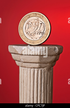Greek € coin on a classical column in front of a red background. The back of the coin is visible on which an owl is shown. Stock Photo