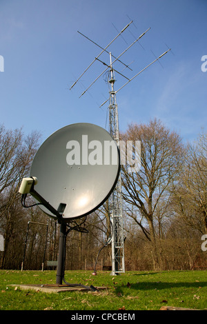 Satellite dish and three element HF radio transmitting mast with Yagi and HF beam Antenna set against a blue sky Stock Photo