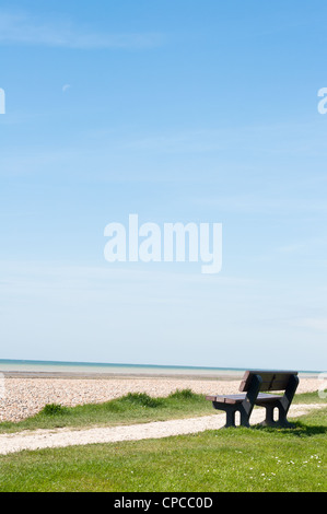 An empty wooden bench on a coastal path, facing the sea with blue sky providing copy space. Stock Photo