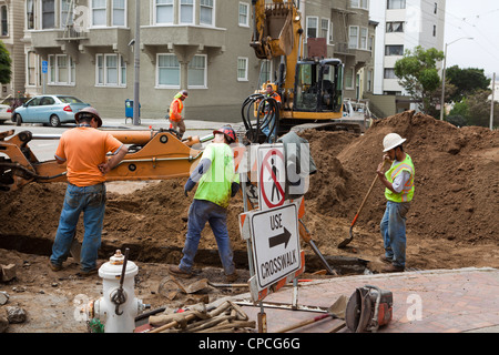 Municipal construction workers and backhoe digging trench Stock Photo