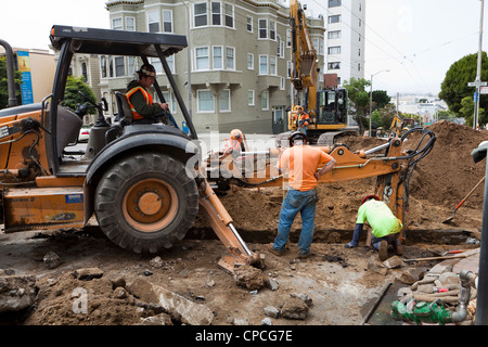 Municipal construction workers and backhoe digging trench Stock Photo