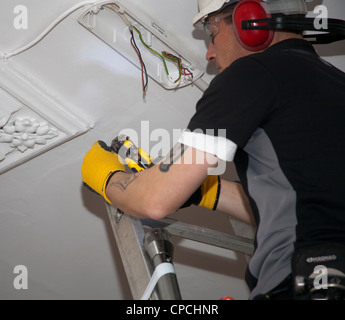 An electrician replacing an emergency light on a ceiling in communal area. Stock Photo