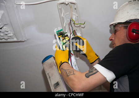 An electrician replacing an emergency light on a ceiling in communal area Stock Photo