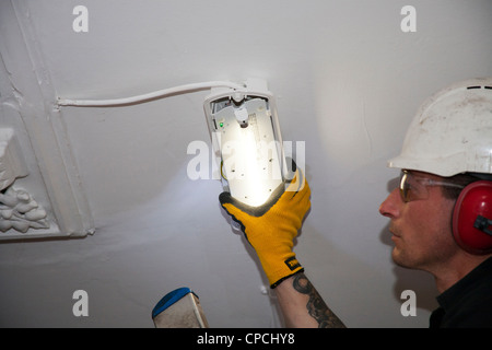 An electrician replacing an emergency light on a ceiling in communal area Stock Photo
