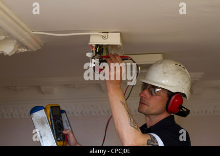 An electrician replacing an emergency light on a ceiling in communal area Stock Photo