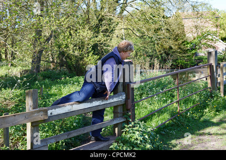 A woman climbing over a stile on the towpath along side the 'River Bure' Norfolk, UK Stock Photo