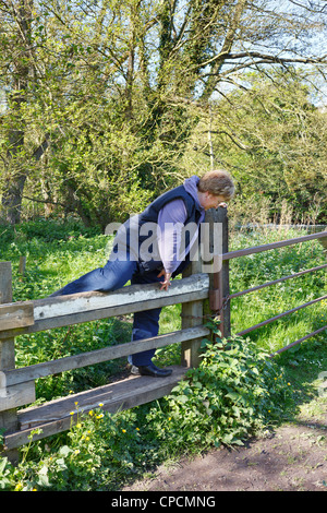 A woman climbing over a stile on the towpath along side the 'River Bure' Norfolk, UK Stock Photo