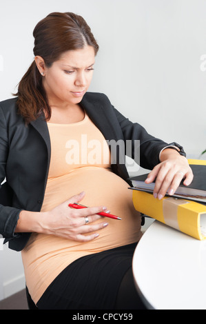 Pregnant woman sitting in an office looking troubled Stock Photo