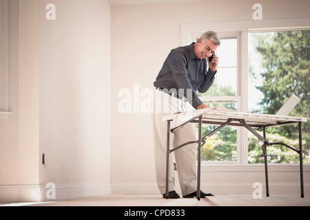 Caucasian man using cell phone and looking at blueprints Stock Photo