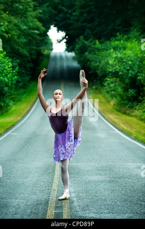 Caucasian ballerina dancing on remote road Stock Photo