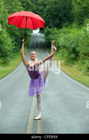 Caucasian ballerina dancing on remote road with umbrella Stock Photo