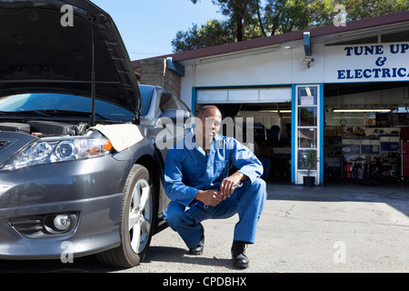 Black mechanic squatting near car Stock Photo