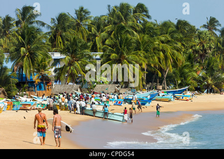 Tourists stroll whilst local fishermen work on this popular surf beach, Arugam Bay, Eastern Province, Sri Lanka, Asia Stock Photo