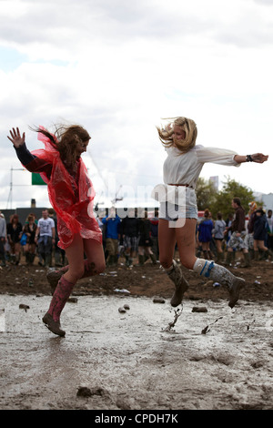 Two girls jumping and playing in the mud at a music festival Stock Photo