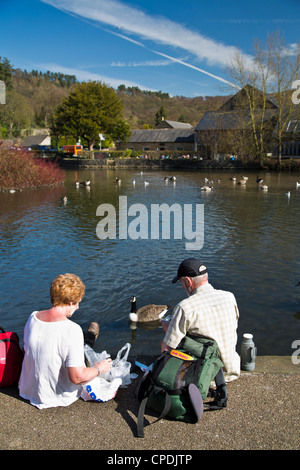 Two people sitting beside river  eating food and  enjoying  fine weather in Bakewell Derbyshire Peak District England Stock Photo