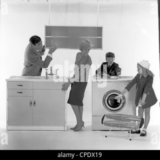 1960s. Photo shoot advertising new kitchen appliances. Mother, father and son and daughter pose in a photographic studio admiring the new  kitchen units and home appliances now available for the modern home. Stock Photo