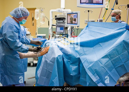 Orthopedic surgeon preparing patient for arthroscopic knee surgery in a hospital operating room suite Stock Photo