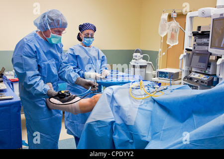 Orthopedic surgeon preparing patient for arthroscopic knee surgery in a hospital operating room suite Stock Photo