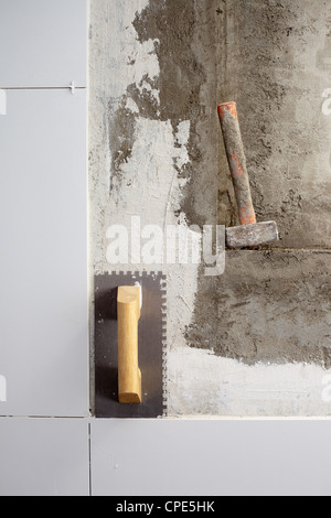 construction tools notched trowel and hammer on tiles mortar wall Stock Photo