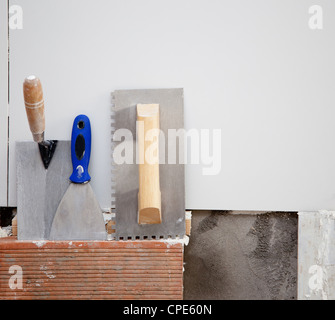 construction tools notched trowel ans spatula on tiles mortar wall Stock Photo