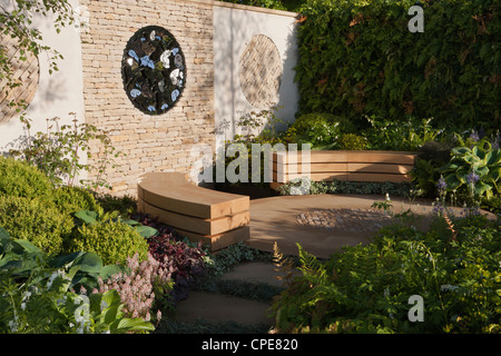 Cottage courtyard garden with cotswold dry stone wall and circular circle patio design area and wooden wood bench benches and a hedge boundary UK Stock Photo