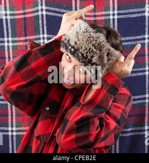 Crazy portrait of a young woman wearing checkered lumberjack shirt and fur hat posing as wild bull. Funny studio shot Stock Photo