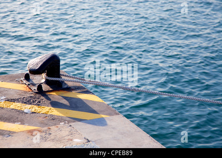 Bollard in port with rope looped around and yellow lines over black Stock Photo
