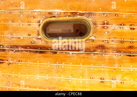 boat oval aged brass porthole in wooden hull with caulking putty and screw Stock Photo