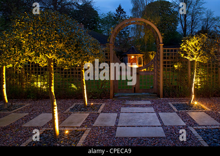 Garden feature Arch at night with holly trees lit and gates leading into lawn area with illuminated Gazebo Stock Photo