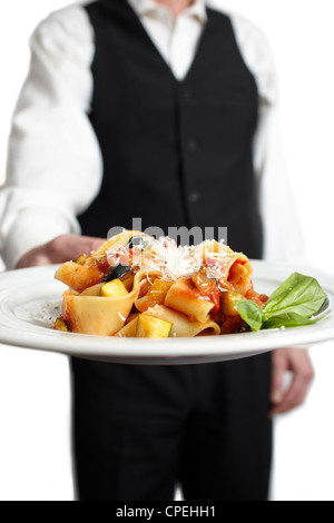 A servant is holding a plate with pasta, tomato sauce, parmesan cheese and basil. Focus on plate. Close-up. Stock Photo